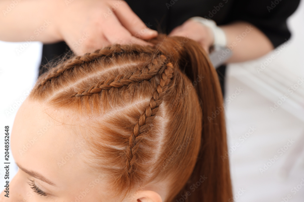 Fototapeta premium Hairstylist braiding teenage girl's hair in salon, selective focus