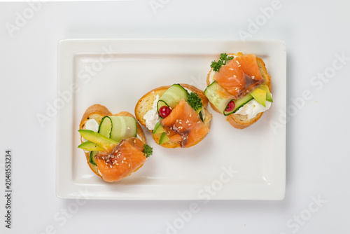 Fotografie Flat lay of three salmon bruschetta appetizers on rectangular plate white backgr