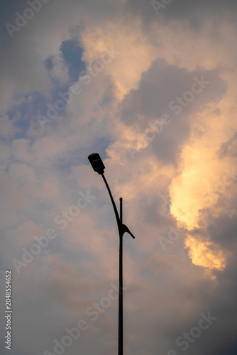 Silhouette of a streetlight against a dramatic sunset sky with clouds.