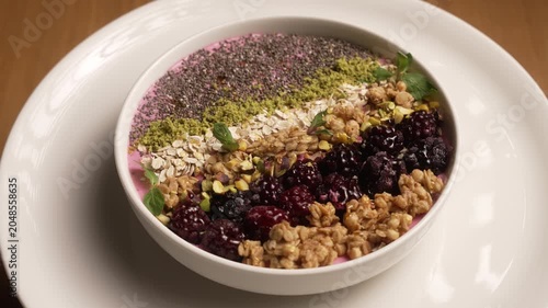 Colorful breakfast smoothie bowl with granola, blackberries, and chia seeds rotating on a plate, fa01
