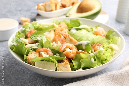 Fotografie Appetizing Caesar salad with shrimps and avocado served on grey table, closeup