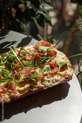 Crispy roman style pizza topped with prosciutto arugula cheese and fresh greens