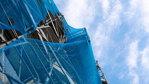 Construction scaffolding with blue safety debris netting on a building site. Architectural metal scaffolding structure for house facade renovation, restoration and industrial development outdoor.