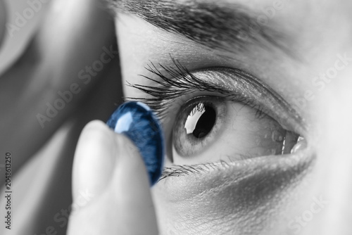 Obraz na plátně Young woman putting in blue contact lens, closeup