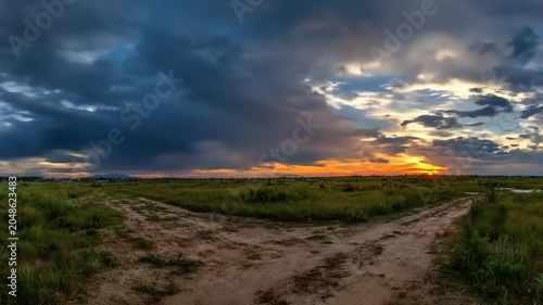 Dramatic sky over open field at sunset with converging dirt paths