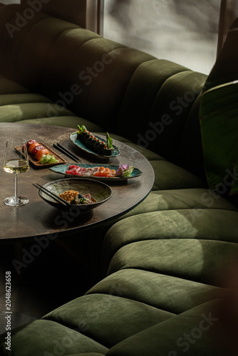 Cuadro en lienzo Japanese restaurant table setup featuring plates of sashimi, nigiri, sushi rolls, tuna tataki, and a glass of white wine