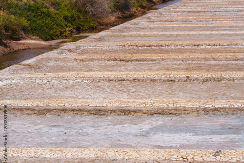 Close view of cracked salt pan beds with a canal running alongside.
