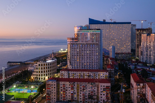 Bild auf Leinwand Horizontal landscape photograph showcasing Batumi's modern high-rise architecture at twilight, featuring a soft pink and purple sunset afterglow over the Black Sea with initial city lights turning on