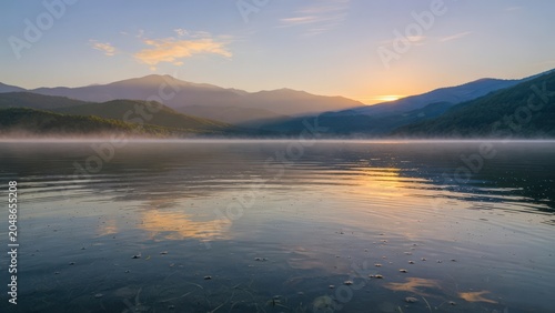 Sunrise Over Misty Mountain Lake With Golden Peaks Reflected in Calm Water