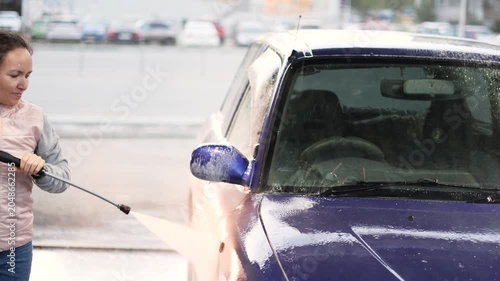 Experience the simple pleasures of life as a woman washes her blue car at a self-service wash. The refreshing spray and bubbly foam make car maintenance a delightful activity. Slow motion 4k video