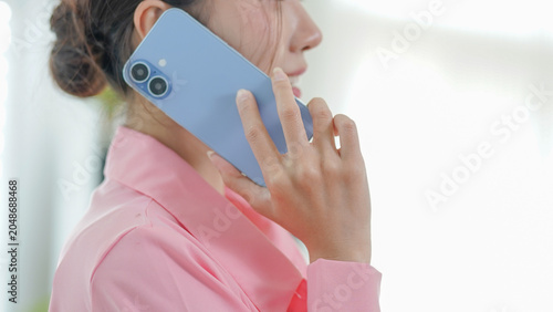 A close-up view of a woman in a pink shirt holding a blue smartphone to her ear during a conversation.