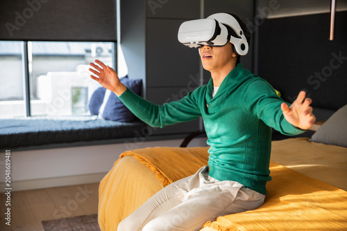White virtual reality headset is resting on bed with mustard-yellow blanket near window seat