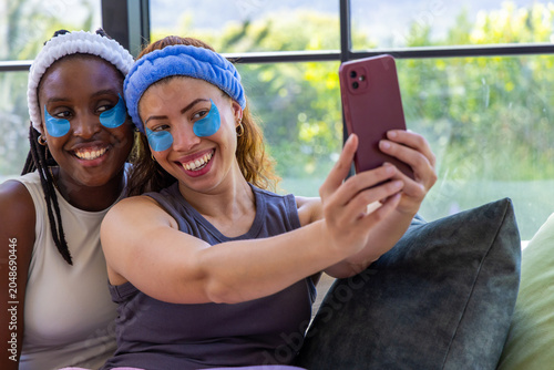 Canvas Print African American female friends taking selfie on sofa wearing headbands and blue