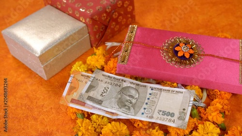 Decorated orange platform with handmade rakhi and other items for Raksha Bandhan celebration. Colorful rakhi with Indian rupee notes  money envelope  marigold flower garland and gifts on the occasi...
