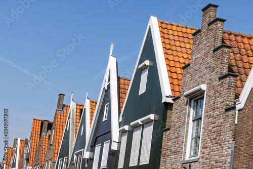 Cuadro en lienzo Volendam, Netherlands: Architectural close-up of a row of traditional Dutch gables, featuring green wooden panels, white trim, and a classic brick step gable against a deep blue sky