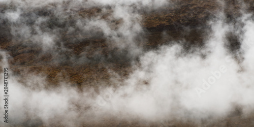 Tableau sur toile Dense white fog blankets a rugged mountainous landscape, obscuring distant peaks and valleys in a natural scene