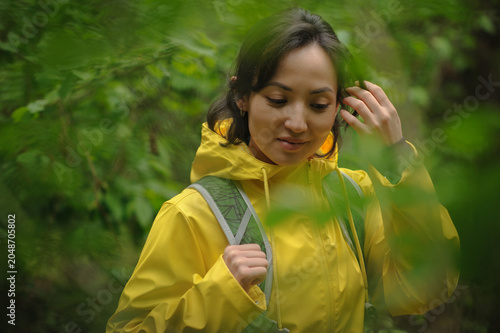 Bild auf Leinwand Portrait of asian tourist in raincoat adjusting hair in forest