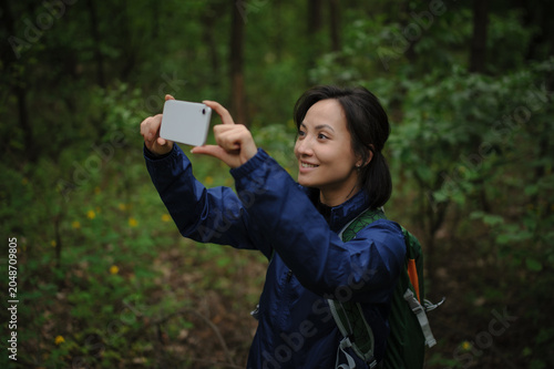 Smiling asian tourist taking photo on smartphone in forest 