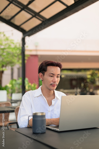 Non-Binary Digital Nomad Coding on Laptop on Office Terrace