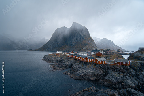 Iconic traditional fishing village of Hamnøy with vibrant red cabins nestled under dramatic mountains and reflected on the calm blue waters of Norway’s Lofoten Islands