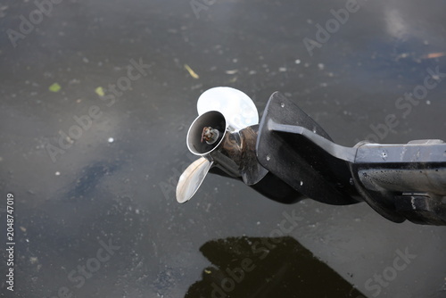 Obraz na płótnie Close-up view of a stainless steel outboard propeller partially submerged above murky water, showing blades, motor housing and reflection