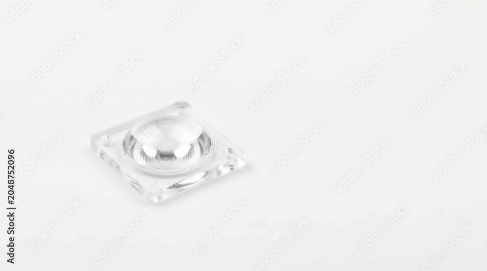 Fototapeta premium Small clear plastic fresnel lens component with a square frame resting on a clean white surface in bright studio lighting