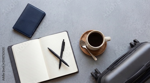 A well-organized travel set-up featuring an open notebook with pens, a cup of coffee, and a suitcase, suggesting preparation for a journey or a productive trip.