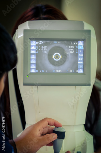 A close-up image of a woman looking at a fractometer eye testing device.