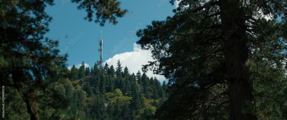 Fototapeta premium Mountain summit antenna surrounded by thick green forest trees