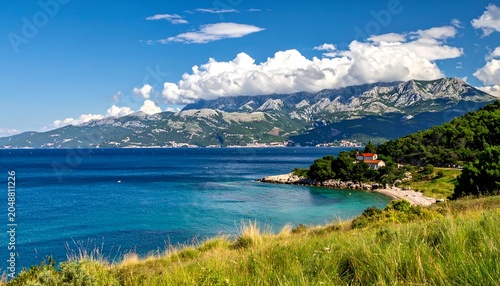 Coastal scene turquoise water, mountain backdrop, green island, grassy foreground, sunny sky