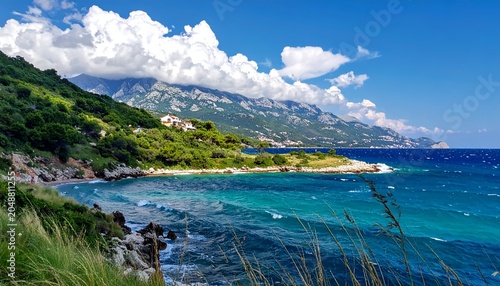 Coastal panorama with mountains, buildings, greenery, and turquoise water under a blue sky