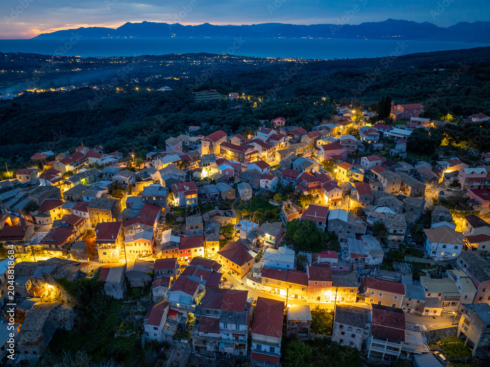 Fototapeta premium Aerial view of Nymfes village edge meeting the dark forest at night, serene travel landscape in Corfu island, Greece