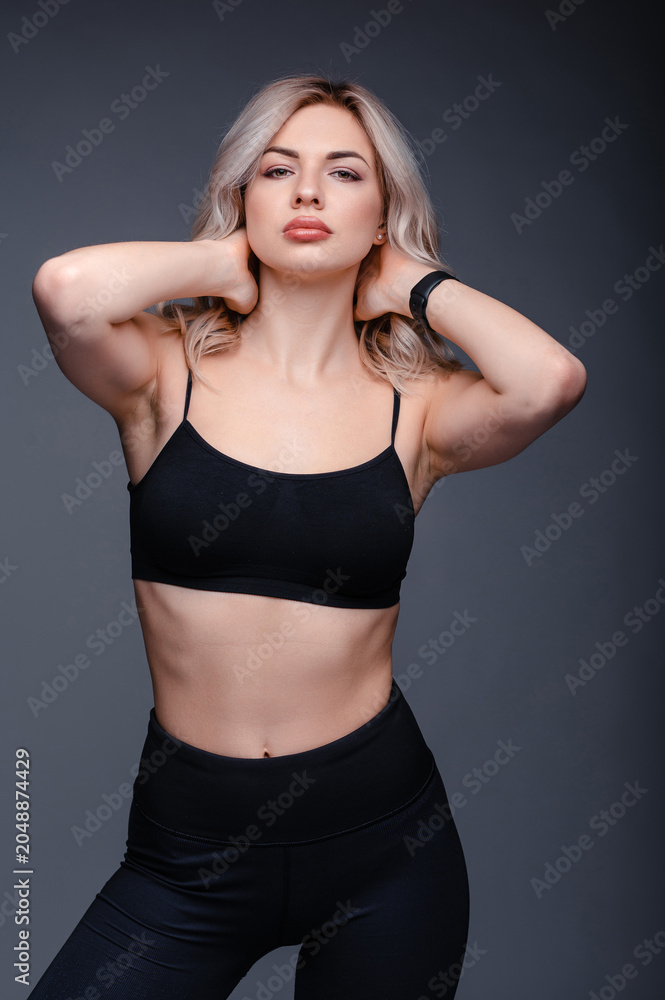 Fototapeta premium Athletic woman with blonde hair in black sportswear posing against a dark background