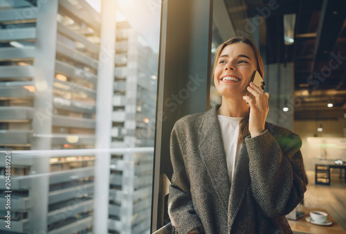 Bild auf Leinwand Happy Caucasian female professional smiles warmly during a phone call in a moder