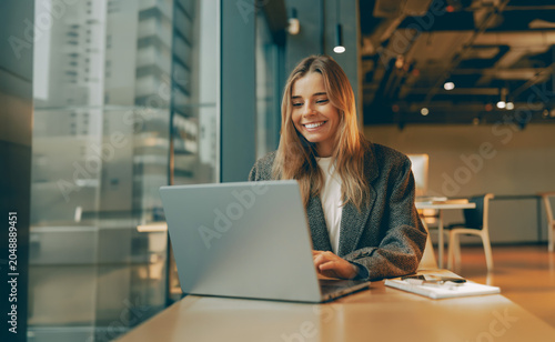 Foto Cheerful Caucasian female entrepreneur working on a laptop under warm natural li