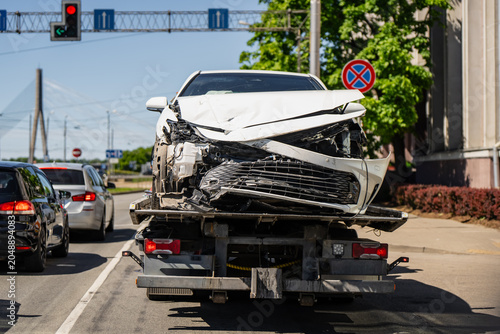 Bild auf Leinwand Damaged automobile with smashed front bumper carried by recovery vehicle on urba