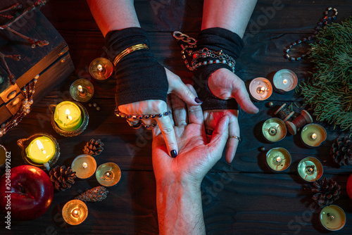 Witch palmistry fortune-telling reading man's palm, witchcrafting, performing ritual among candles, pumpkins. Magician Halloween night