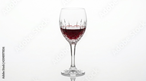 Elegant cut crystal wine glass filled with a serving of rich red wine, isolated on a seamless white background.