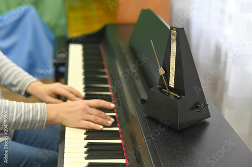 Female hands playing electronic piano with metronome, focusing on rhythm and precision. metronome ensures perfect timing, while piano allows for creative expression and musical discipline.