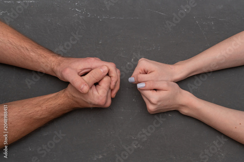 Male joined hands confront female closed hands on dark stone background. Strong defensive concept represents relationship conflict resolution. People fight for gender equality partnership mood.