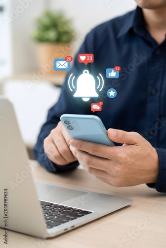 Man receiving social media notifications on smartphone while working on laptop indoors