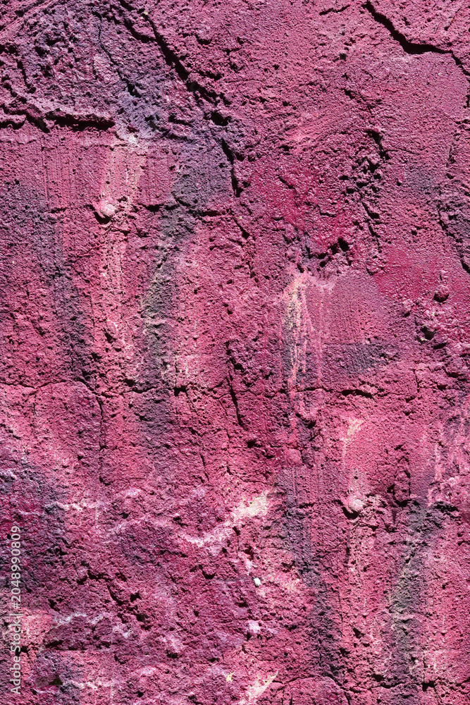 Fototapeta premium Full frame view of a weather damaged purple plaster wall showing rough uneven texture cracks and dark stains.