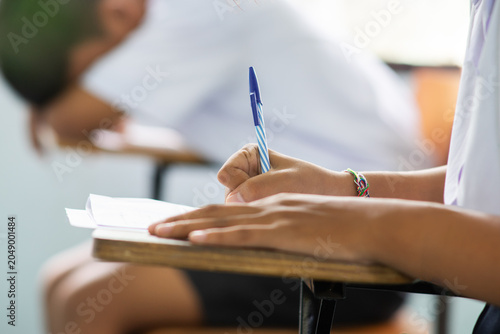 Close-up of Student Writing Exam with Classmate Sleeping in Background