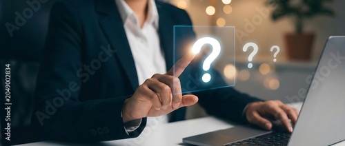 Businessperson using a laptop while pointing to question marks on a virtual screen
