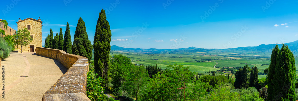 Naklejka premium Wide panoramic view of the hills and countryside surrounding the village of Pienza (Tuscany village, Italy) seen from its medieval fortified walls, during early summertime.