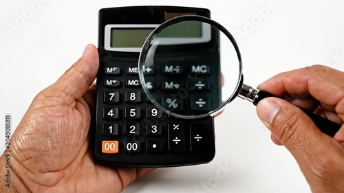 Hand using magnifying glass to inspect digital calculator.