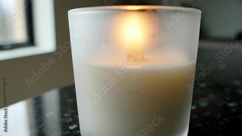 Close Up of a Burning Candle in a Frosted Glass Holder on a Granite Surface