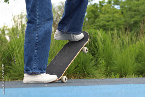 Low angle view of a person in jeans and white sneakers balancing on a skateboard, close-up. Active leisure and modern culture. Young woman skateboarding in the summer. Street sport concept