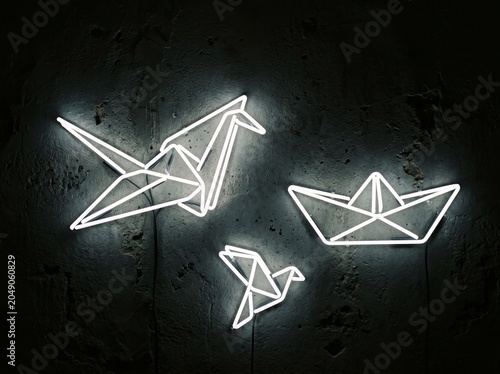 Minimalist neon origami cranes and boats made of glowing white wire on dark textured background
