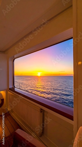 Interior view of window framing a vibrant sunset over a tranquil ocean